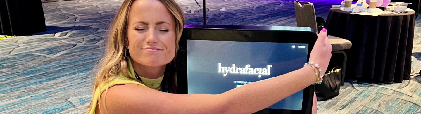 Woman enthusiast embracing the Hydrafacial machine at an event, showcasing excitement and affection