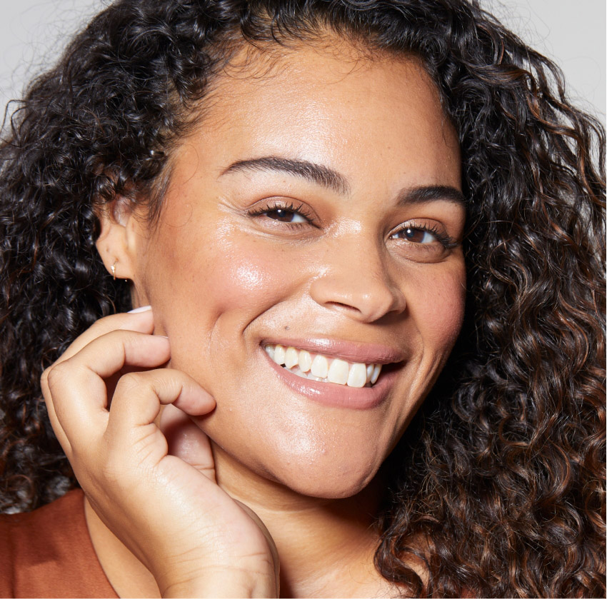 Smiling woman with curly hair, showcasing her glowing and healthy skin